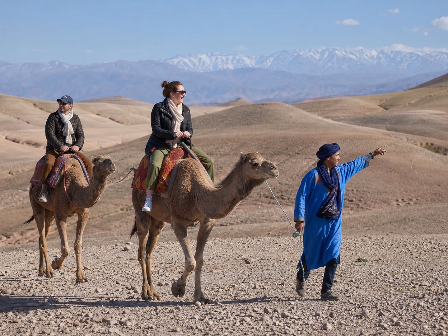 Travellers riding dromedaries with a local guide across Agafay's rocky hills